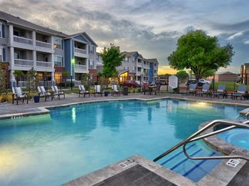 A swimming pool surrounded by lounge chairs and apartment buildings in the background.